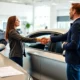 Customer shaking hands with car dealer in a modern showroom with embedded auto insurance documents on table