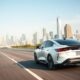 Hybrid car driving on a U.S. highway with city skyline in 2025.